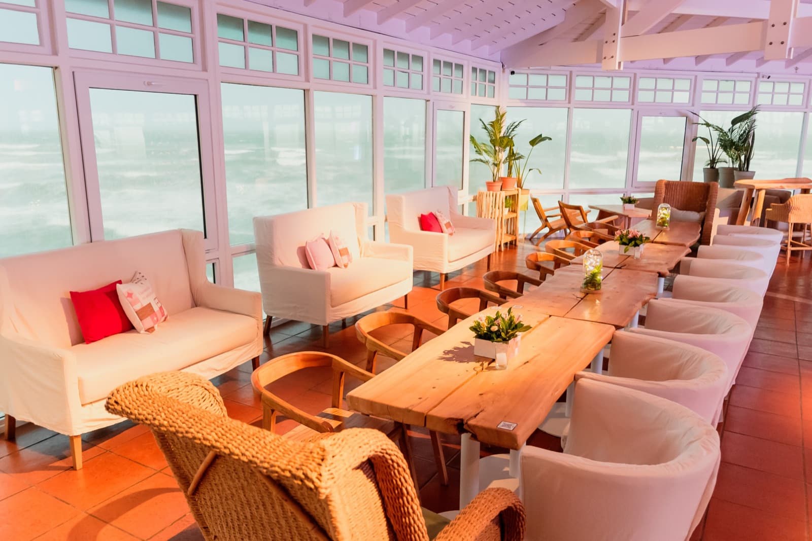 El salón de día, con sillones blancos y una mesa larga de madera frente a los ventanales que dan al mar.
