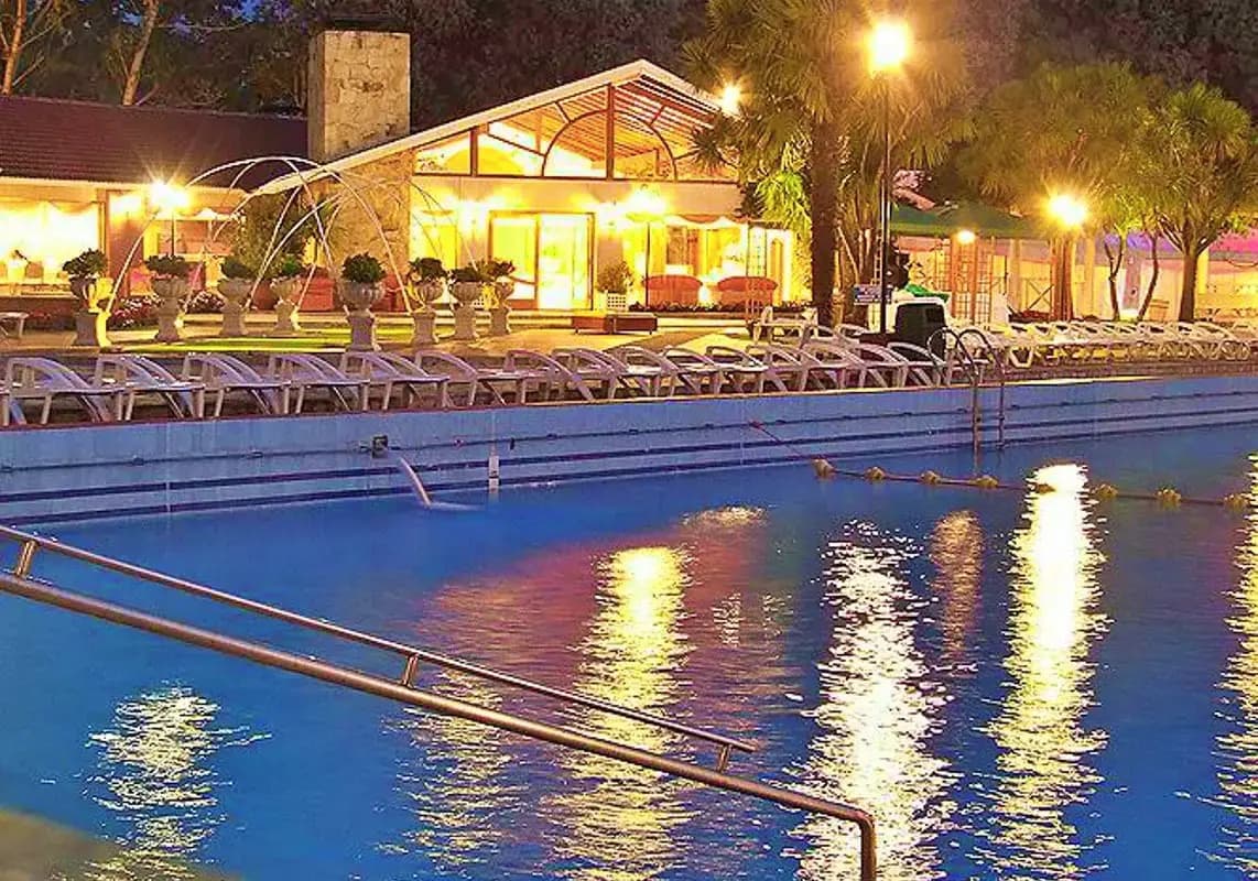 La pileta del parque de noche con las luces del salón reflejadas en el agua y las reposeras alineadas en el borde.
