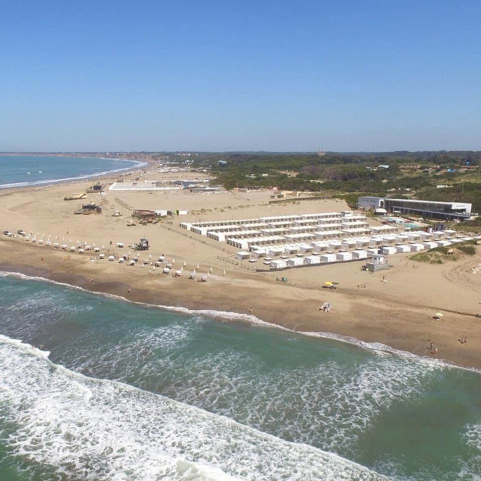 El balneario desde el aire, con las hileras de carpas blancas sobre la arena y la rompiente del mar en primer plano.