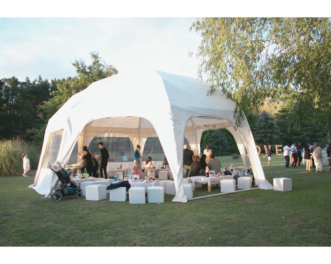 La carpa beduina blanca armada sobre el césped del parque, con puffs alrededor y los invitados dispersos a lo lejos.