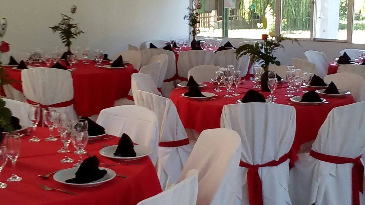 El salón con las mesas redondas vestidas de rojo, las sillas con fundas blancas y las ventanas al parque de fondo.