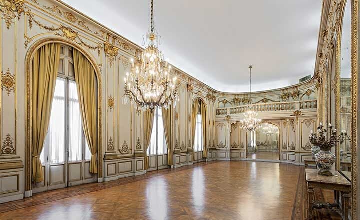 El salón de baile vacío, con piso de parquet lustrado, arañas de caireles, cortinas doradas en los ventanales y molduras blancas y oro en las paredes.