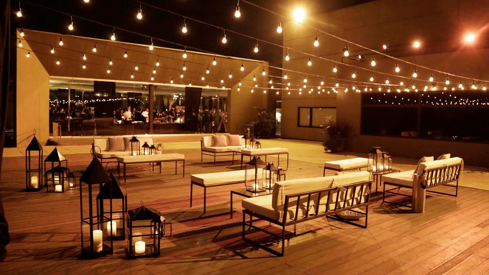 El deck de madera armado como living, con sillones claros, mesas bajas y faroles con velas, bajo guirnaldas de luces colgadas de punta a punta.