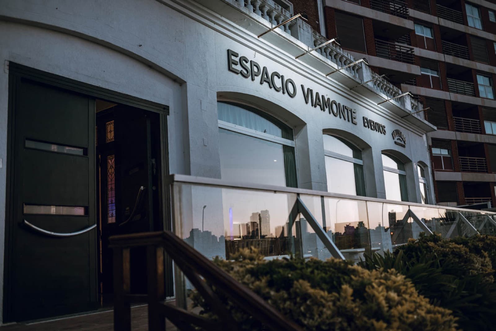 El frente del salón con el nombre en letras sobre la fachada blanca y la baranda de la terraza adelante.