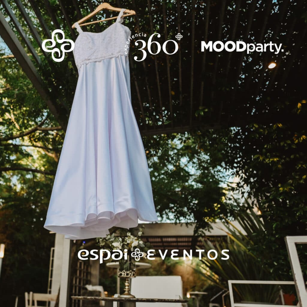 Un vestido de novia colgado de una percha bajo la pérgola, con los árboles y las luces del jardín detrás.