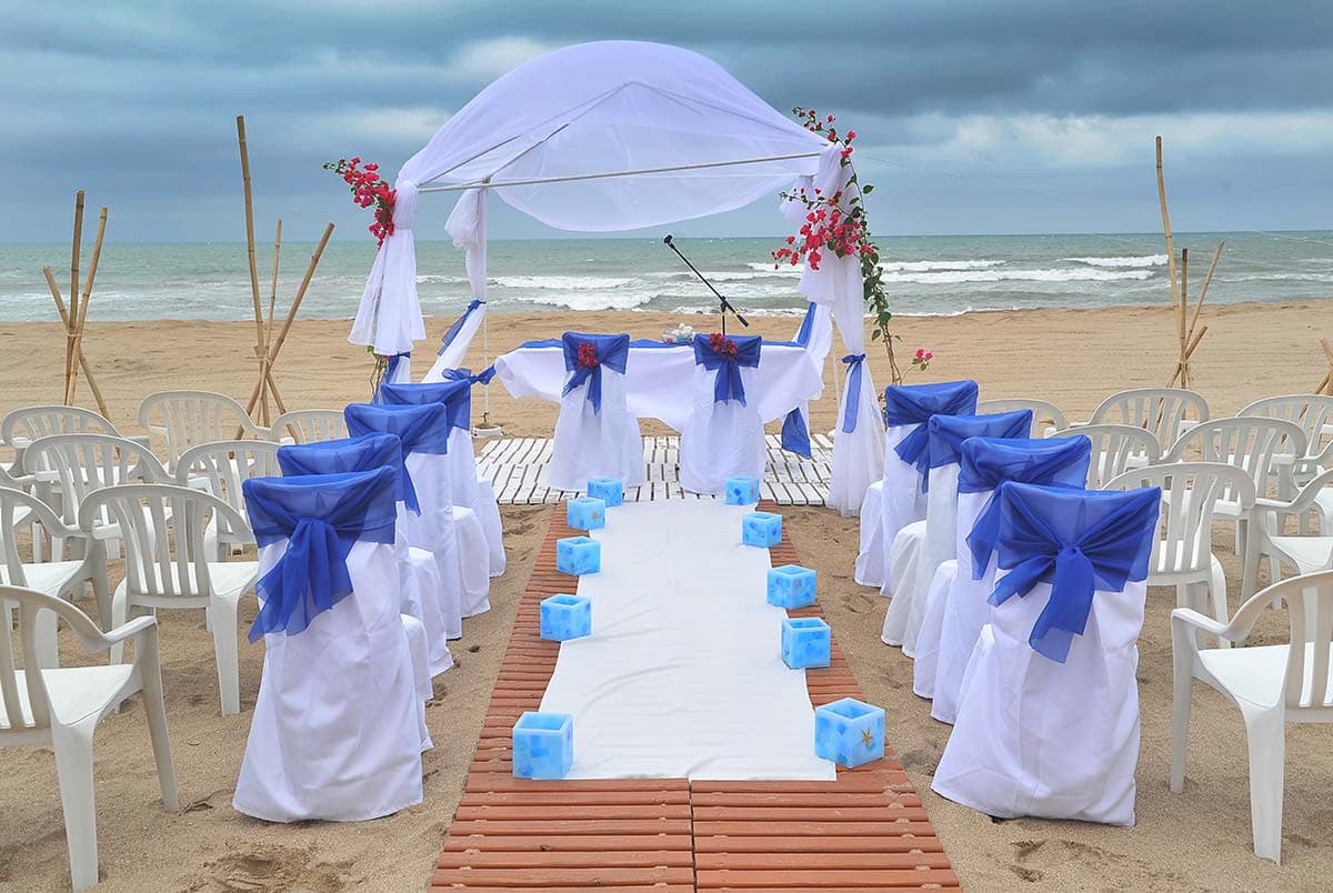La ceremonia armada sobre la arena: el altar con telas blancas frente al mar, la alfombra y las sillas con moños azules a los costados.