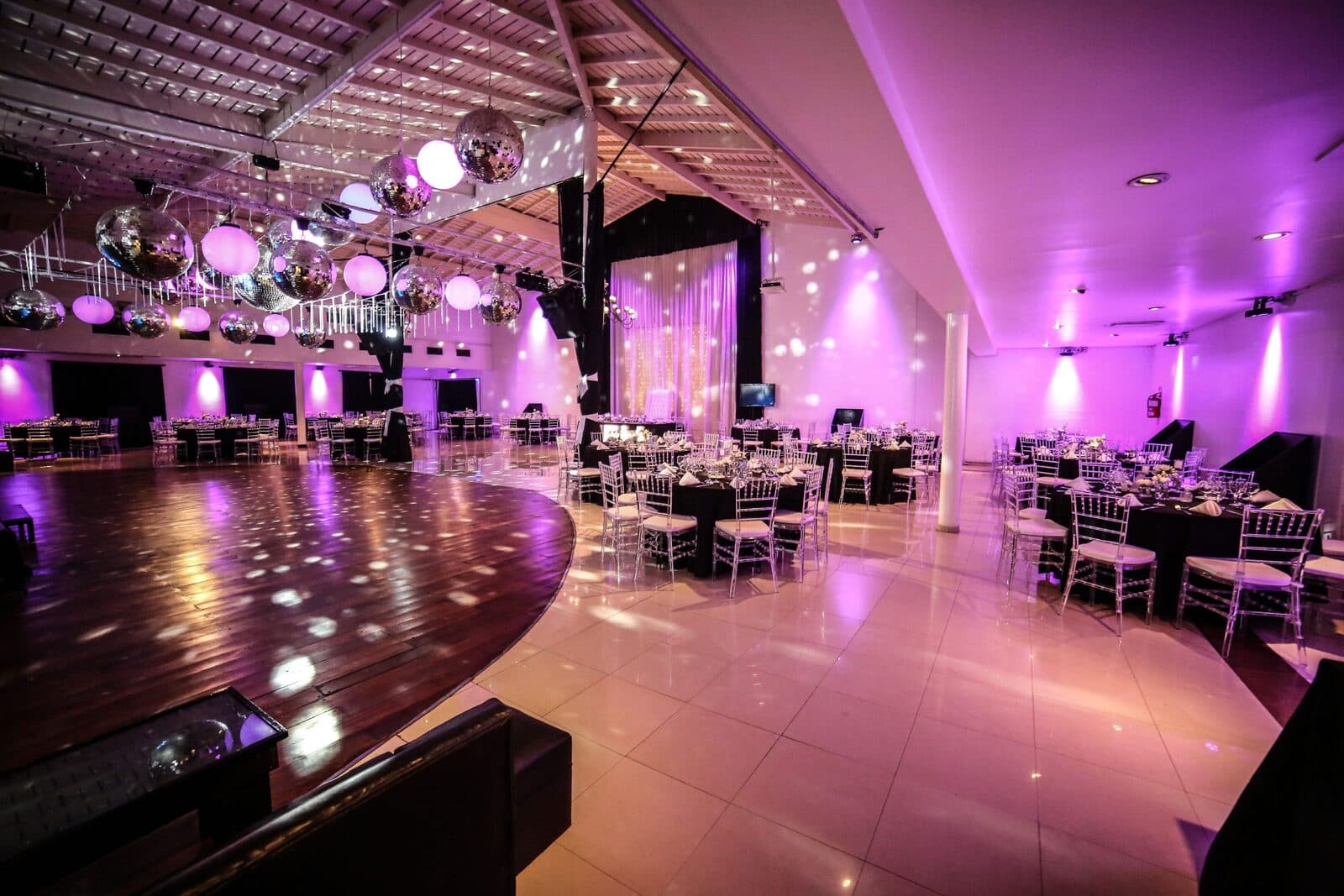 La pista de baile de madera vacía, con las mesas alrededor y bolas de espejo y globos colgando del techo bajo luz magenta.