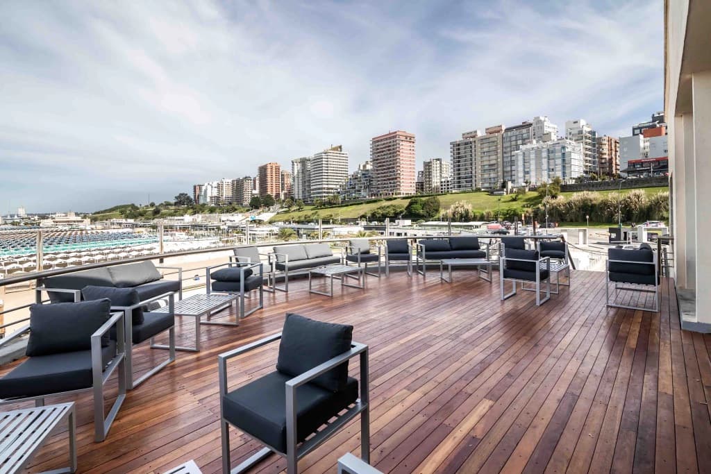 La terraza de madera con sillones bajos, mirando al balneario de Playa Grande y a los edificios de la ciudad al fondo.