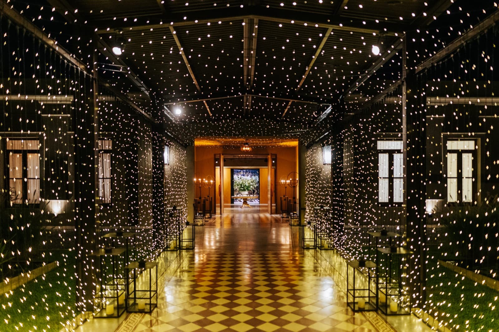 La galería del salón de noche, con cortinas de luces colgando de punta a punta a los dos lados y el piso de damero reflejando las velas.