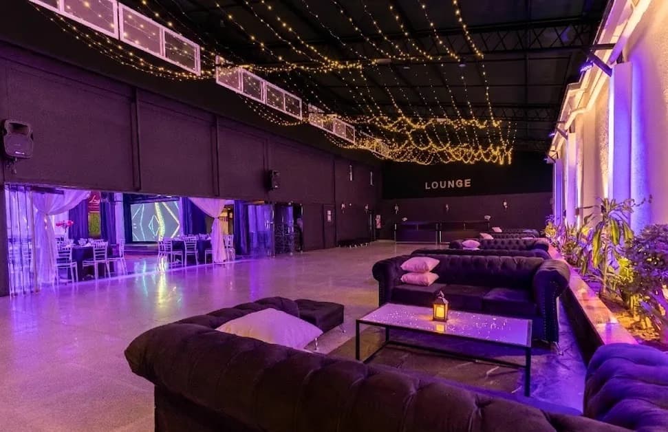 El sector de recepción con sillones capitoné oscuros, almohadones y mesas ratonas bajo guirnaldas de luces cálidas, y el cartel LOUNGE en la pared del fondo.