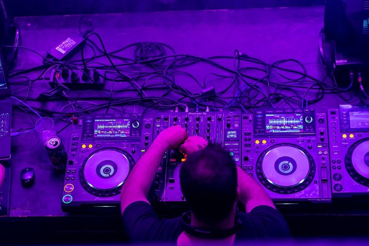La consola de DJ vista desde arriba, con las bandejas iluminadas de violeta y los cables sobre la mesa.