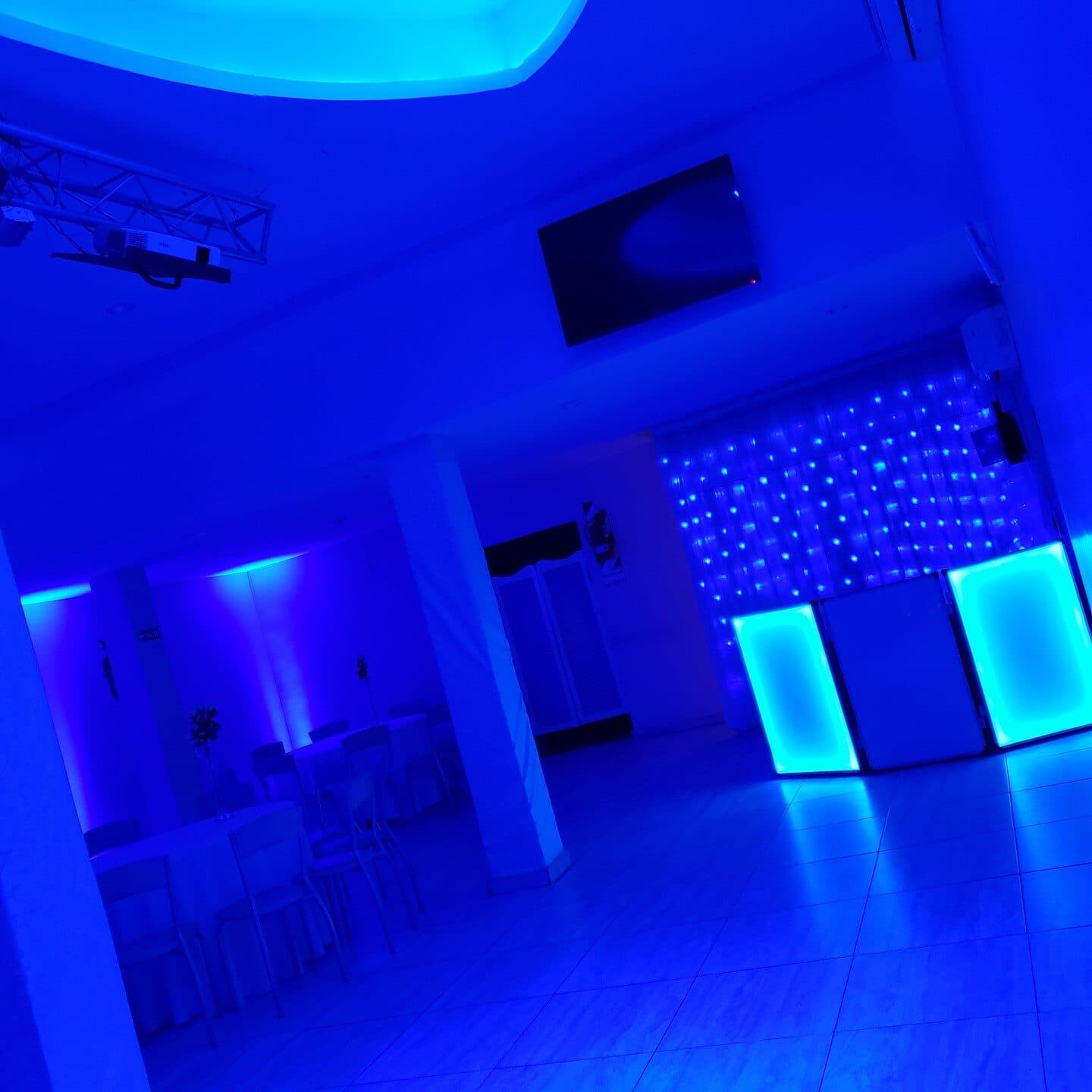 La pista vacía iluminada de azul, con la cabina de sonido y una pantalla de leds al fondo, sillas transparentes contra la pared y cortinados claros.