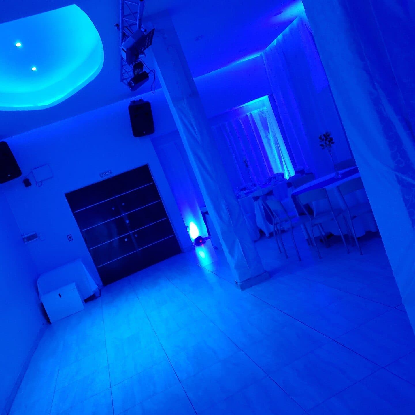 El salón vacío con luz azul, la barra contra la pared, el piso claro reflejando y el sector de mesas altas al fondo.