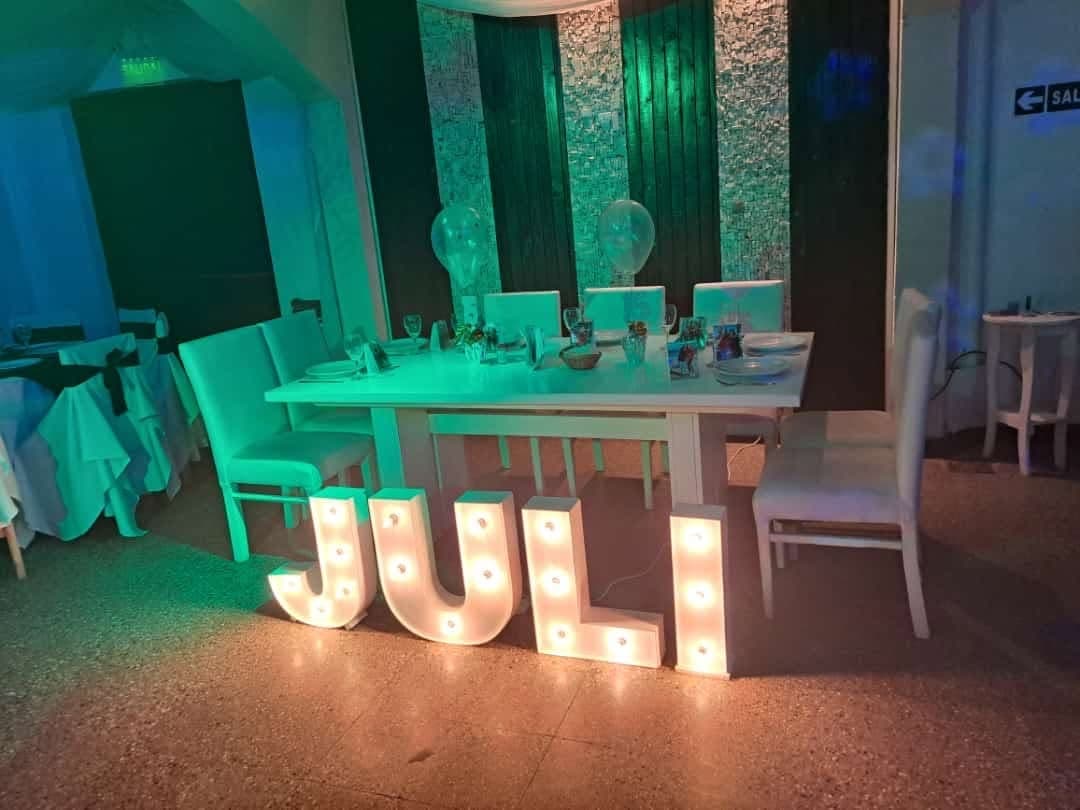 La mesa principal del salón con las letras luminosas del nombre adelante y la pared de lentejuelas iluminada de verde.