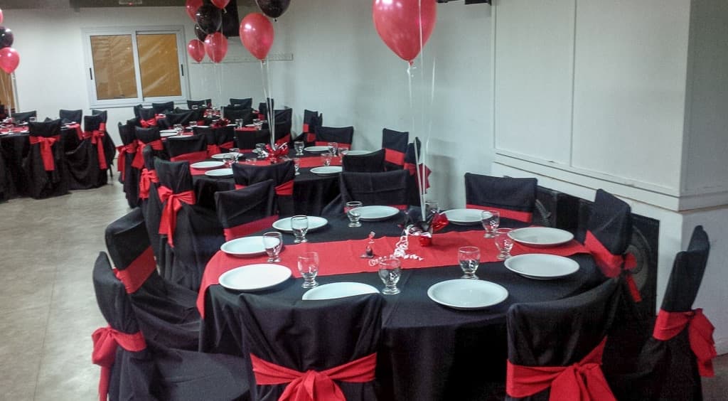 El salón con las mesas redondas vestidas de negro y rojo, las sillas con moños y globos atados sobre cada mesa.