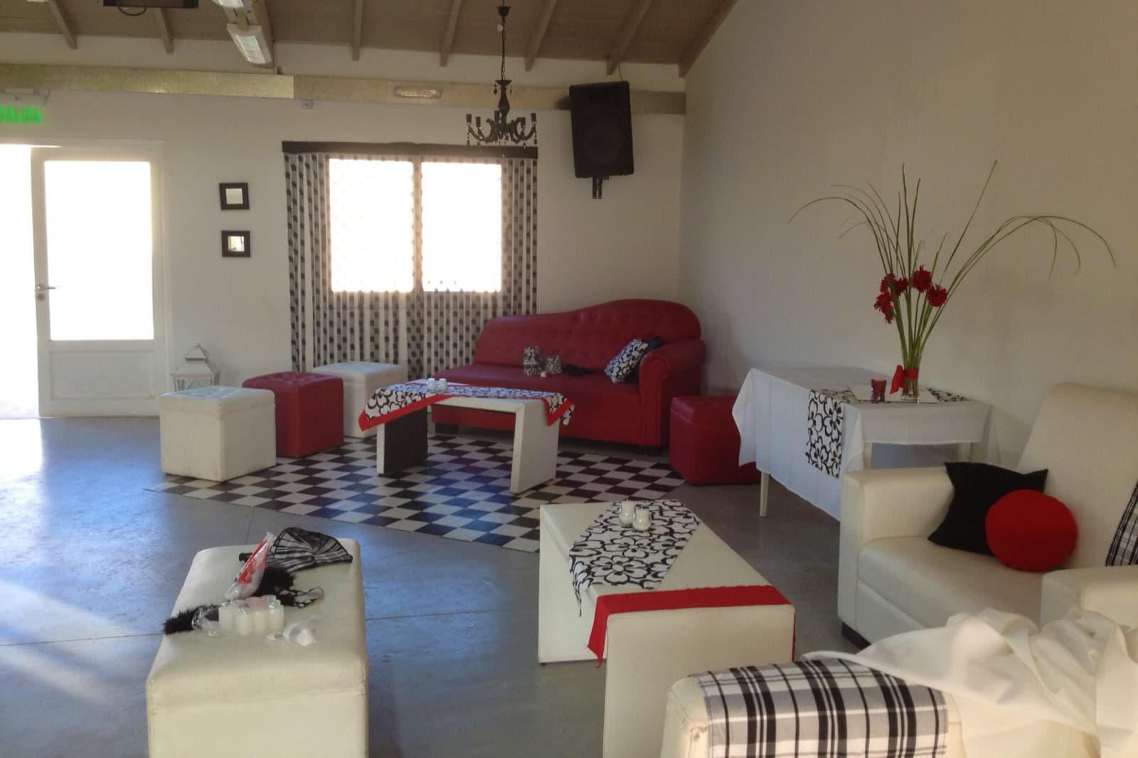 El sector de living con puffs blancos, sillones rojos y el piso damero, con la ventana al fondo.