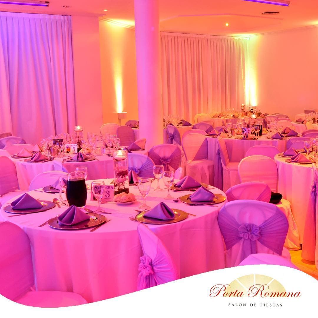 Las mesas servidas bajo luz rosa y violeta, con servilletas en punta sobre platos de presentación dorados, velas flotantes y los cortinados iluminados detrás.