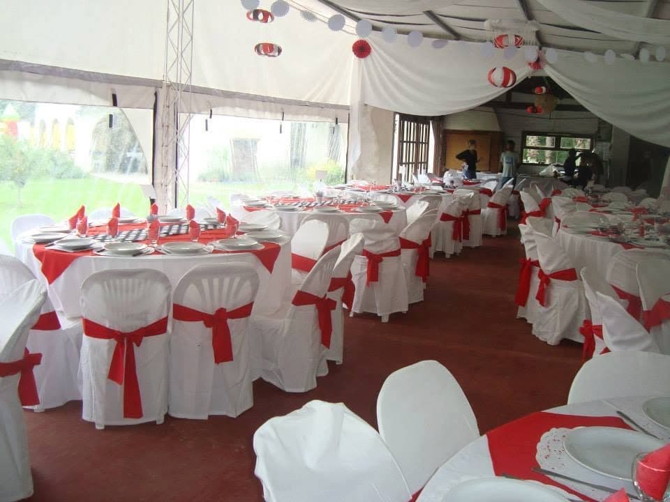 El salón bajo la carpa con las mesas redondas vestidas de blanco y rojo y los ventanales al parque.