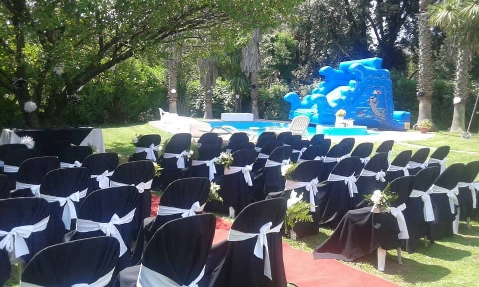Las sillas de la ceremonia alineadas sobre el césped con fundas azules y moños blancos, y la pileta al fondo.