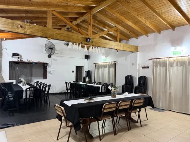 El salón vacío y puesto, con el techo de madera a dos aguas, las mesas vestidas de blanco y negro y el piso de baldosas claras.