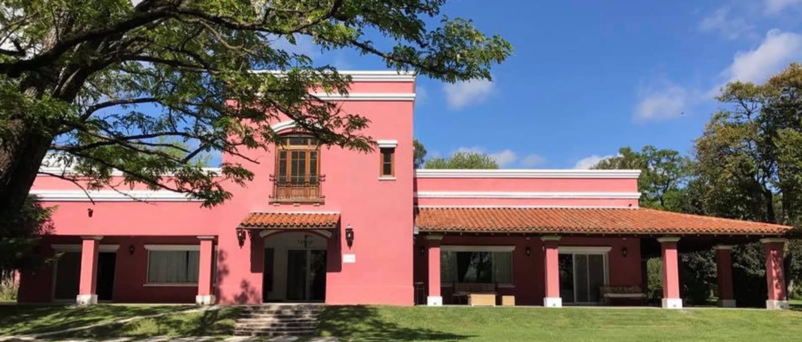 La casona rosada de la quinta vista desde el parque, con la galería de columnas y un árbol grande en primer plano.