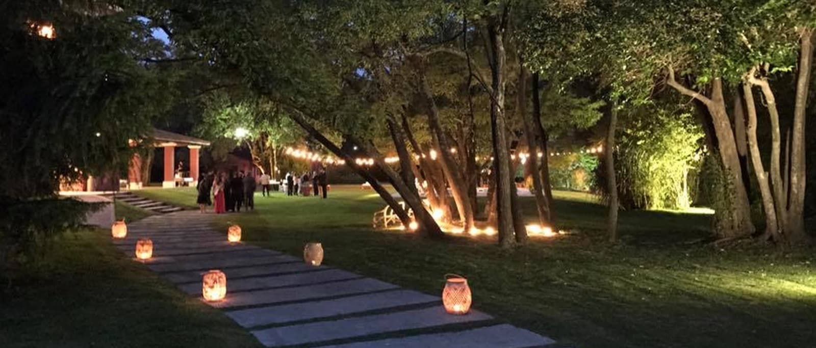 El camino de losas iluminado de noche con faroles de papel a los costados y los árboles del parque encendidos por abajo.