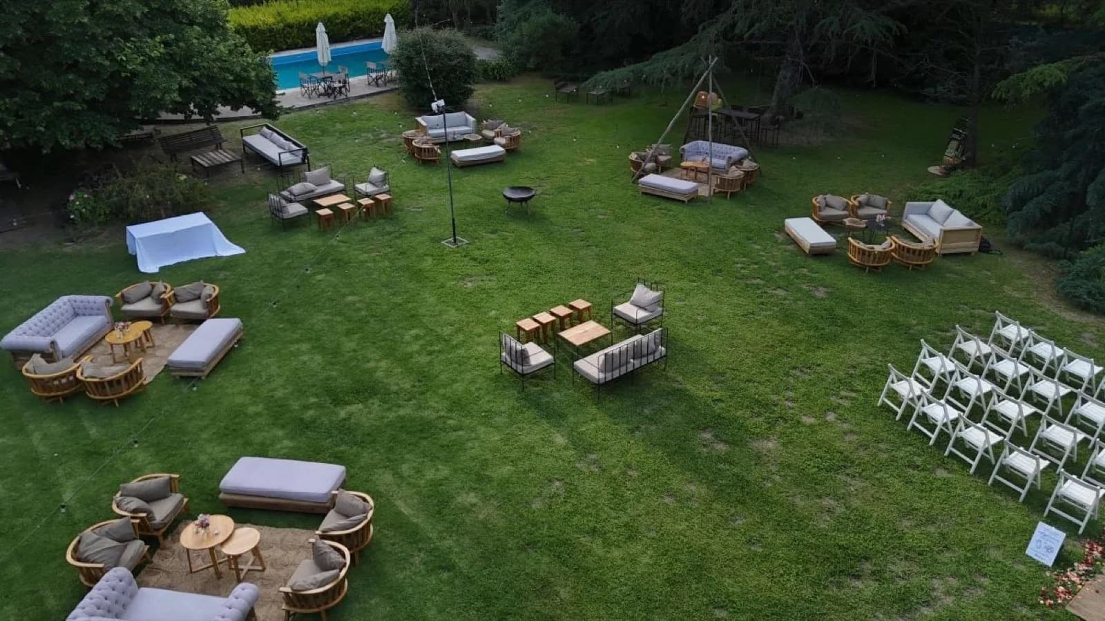 Vista aérea del parque de la quinta puesto para una fiesta, con livings, sillas de ceremonia y la pileta al fondo.