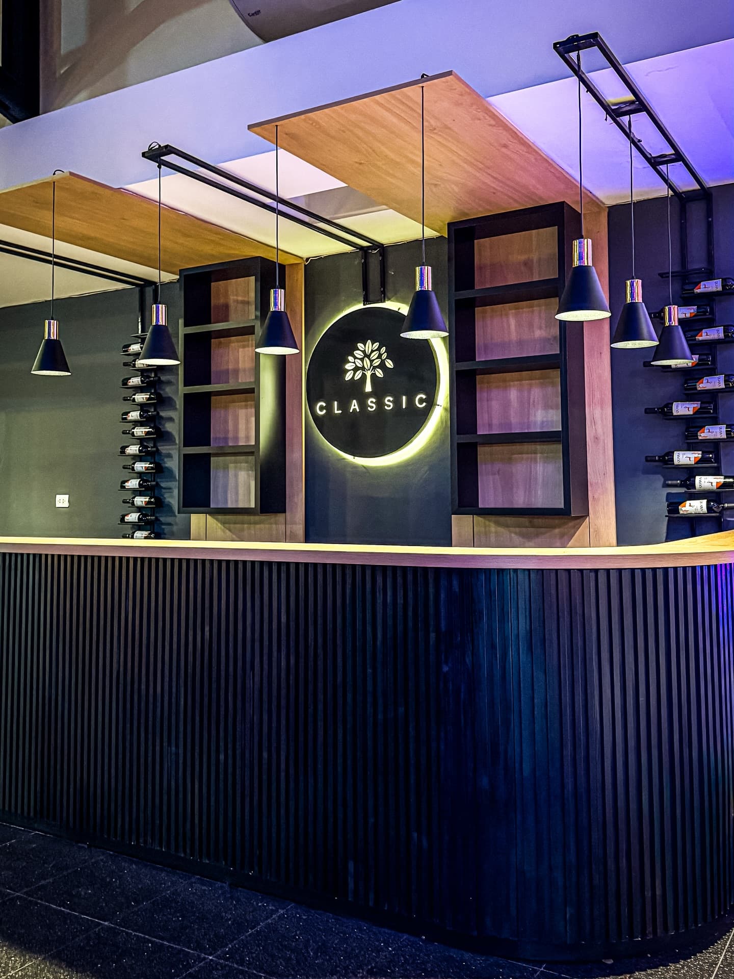 La barra del salón, con frente de listones de madera oscura, botelleros a los costados y el logo del lugar iluminado en la pared del fondo.