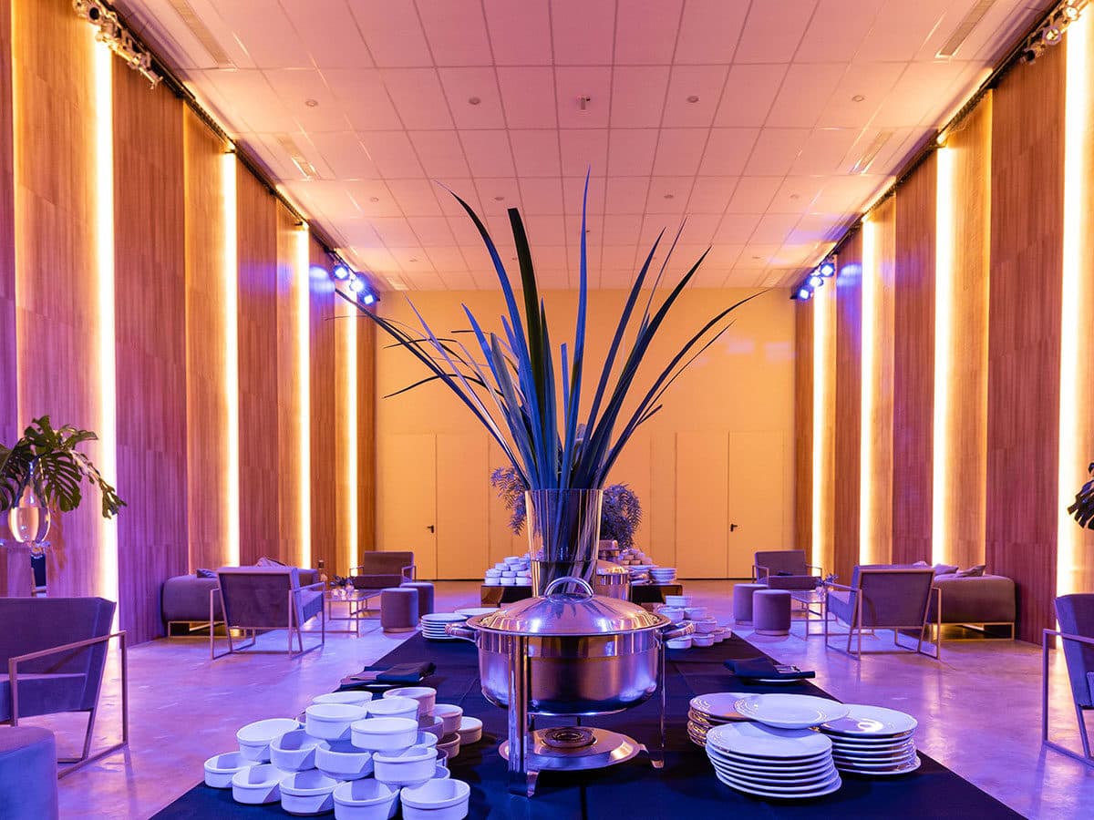 El salón con las columnas de madera iluminadas de amarillo a los dos lados, sillones bajos contra las paredes y una mesa de buffet con vajilla apilada en el centro.
