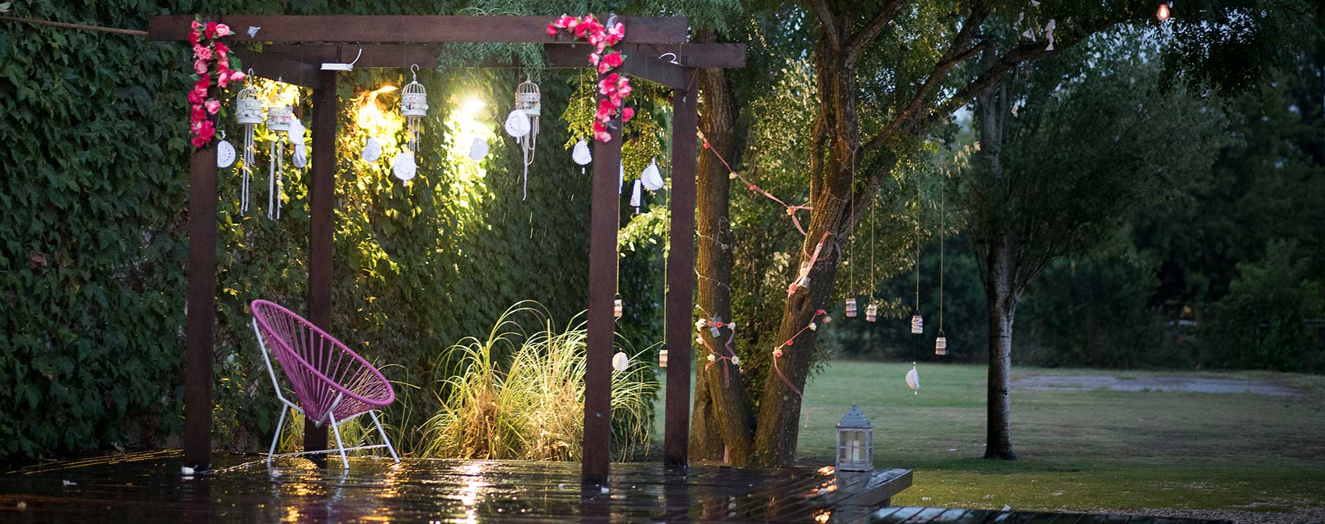 El parque de día, con una pérgola de madera cubierta de enredadera, césped y árboles alrededor.