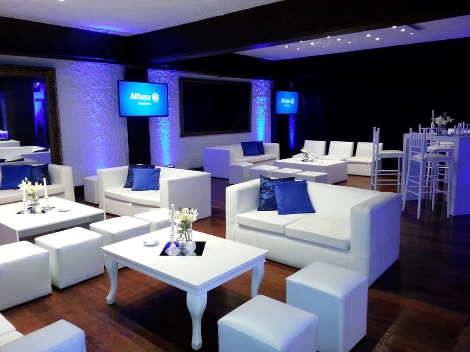 El salón El Dorado armado con livings blancos y almohadones azules, iluminado de azul contra la pared de piedra.