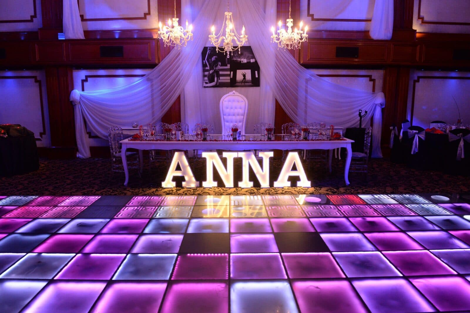 La pista de vidrio encendida en violeta y rosa, con la mesa principal al fondo bajo cortinas blancas y letras luminosas sobre ella.