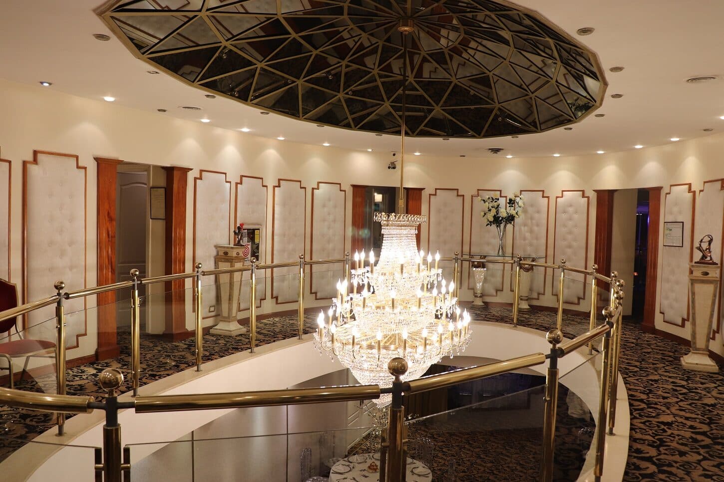 El hall de entrada con una araña de caireles colgando de la cúpula vidriada y la baranda de bronce del entrepiso alrededor.